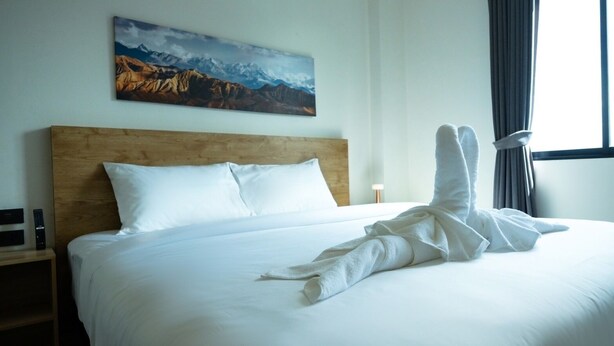 A hotel room with a large bed, a wooden headboard, a painting of mountains, and a window with curtains. - Double J Hotel (Chiang Mai)