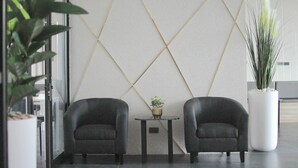A modern lobby with two black armchairs, a small table with a plant, and a decorative wall with geometric patterns. - Double J Hotel (Chiang Mai)