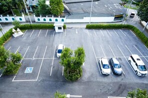 Ein Parkplatz mit markierten Stellplätzen, darunter ein Stellplatz für Menschen mit Behinderung, umgeben von Grünflächen und Gebäuden im Hintergrund.
