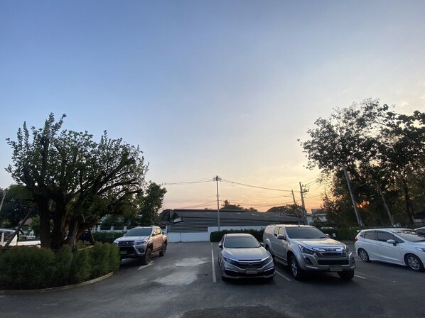 A parking lot with several cars, trees, and a building in the background. - Double J Hotel (Chiang Mai)
