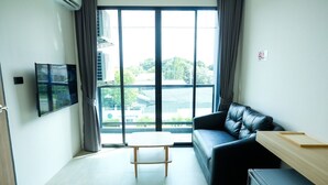 A modern living room with a black leather sofa, a wooden table, and a TV mounted on the wall. - Double J Hotel (Chiang Mai)