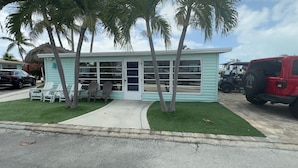 A small, light blue building with a covered outdoor seating area, palm trees, and a red Jeep parked nearby.