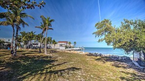 A coastal property with a grassy lawn, palm trees, and a view of the ocean.