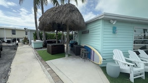 A beach house with a thatched roof, outdoor seating, and a surfboard.