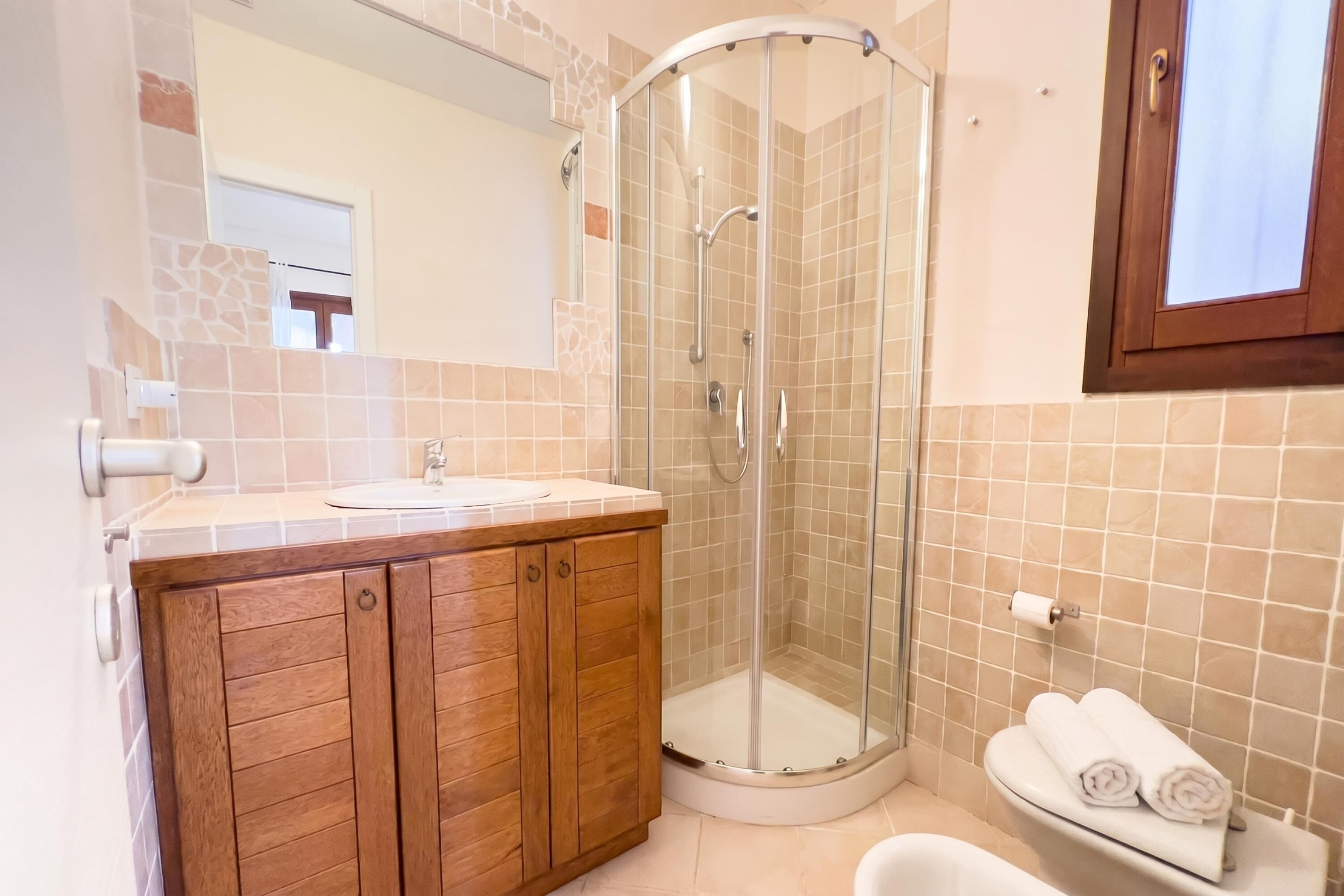 A bathroom with a glass shower enclosure, wooden vanity, and a toilet with a towel rack.