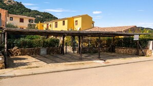 A yellow building with a stone wall and a covered area with a gate. - Il Glicine 1.5 Km From The Beach, Vaccileddi, Italy (Vaccileddi)