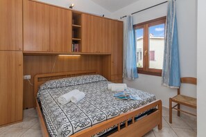 A bedroom with a bed, wooden wardrobe, and a window with curtains.
