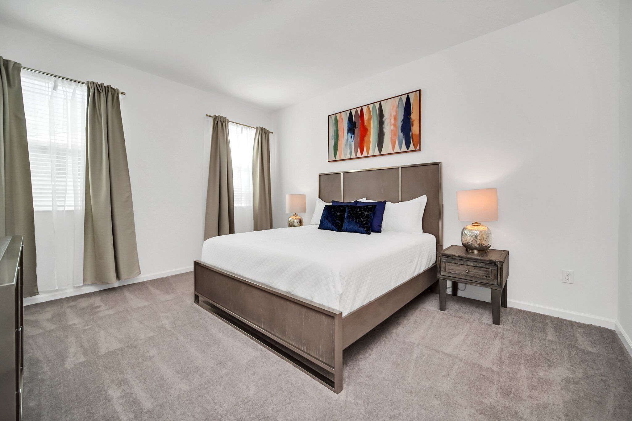 Une chambre à coucher avec un grand lit, deux tables de chevet avec des lampes, une tête de lit et un tableau au mur.