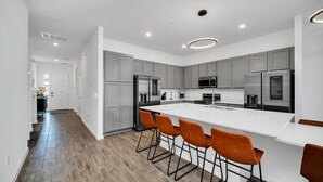 A modern kitchen with grey cabinets, stainless steel appliances, and a white island with orange bar stools.