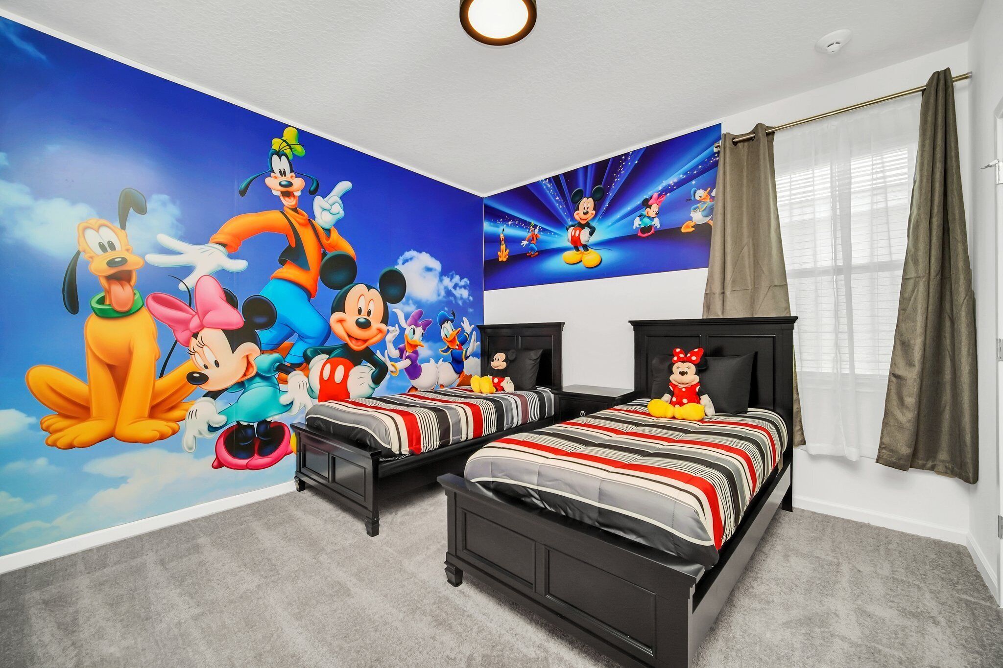 A bedroom with two beds, a large Disney-themed mural on the wall, and a window with curtains.