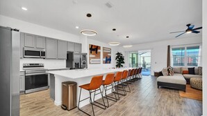 A modern kitchen with a central island, stainless steel appliances, and a seating area with orange chairs.