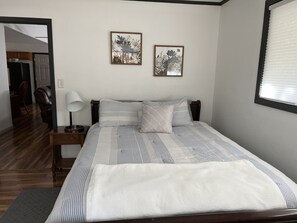Ein ordentlich bezogenes Bett mit Streifenmuster, ein Nachttisch mit Lampe sowie zwei gerahmte Blumenbilder an der Wand.