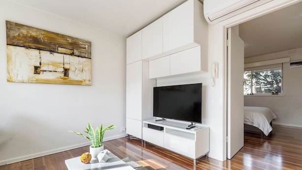 Un salon moderne avec un téléviseur à écran plat posé sur un meuble de télévision blanc, une table basse agrémentée d’une plante et un tableau accroché au mur.