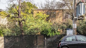 Une voiture noire est garée à côté d’une clôture noire, avec un bâtiment en arrière-plan.