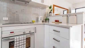 Une cuisine moderne avec des meubles blancs, une hotte en acier inoxydable, un four encastré et un plan de travail agrémenté d’une bouilloire, d’un bol et d’une plante.
