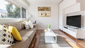Un salon moderne avec un canapé, une table basse, un téléviseur et des œuvres d’art accrochées au mur.