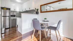 Une cuisine moderne avec des meubles blancs, un réfrigérateur en acier inoxydable, un four à micro-ondes et un évier. On y trouve également un coin repas avec une petite table et deux chaises.