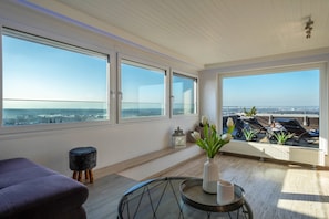 Een ruim balkon met uitzicht op de stad, een ronde tafel met een vaas, en een paarse bank.