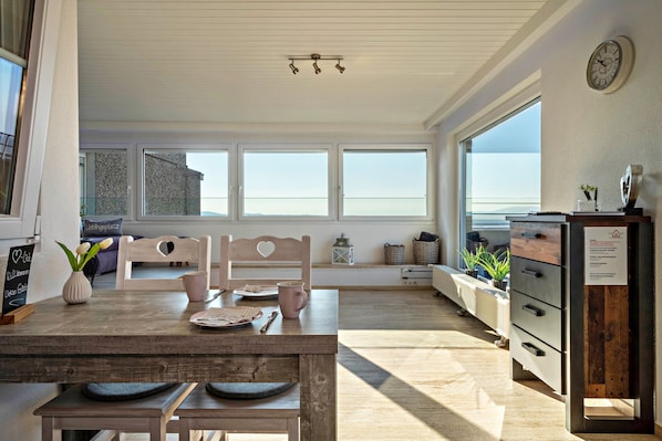 Een moderne keuken met een houten tafel, stoelen en uitzicht op zee door grote ramen.