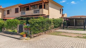 Una casa de dos pisos con un balcón, un espacio de estar al aire libre cubierto y un camino de entrada pavimentado.