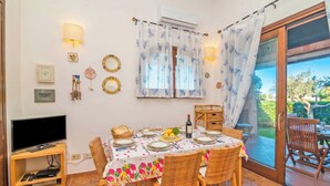 Un coin repas avec une table dressée pour quatre personnes, un téléviseur posé sur un meuble et une porte-fenêtre coulissante donnant sur l’extérieur.