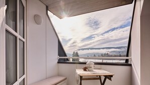 Un balcone con vista su un lago e montagne, un tavolo di legno con un vaso e una panca.