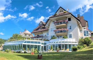 Une grande maison à étages dotée d’une véranda en verre, d’un balcon orné de fleurs et d’une enseigne indiquant le nom « Sunside ».