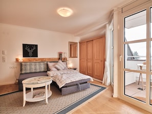 Une chambre à coucher comprenant un lit, une table de chevet, une lampe, un tableau, une armoire et une vue sur l’extérieur, visible à travers une porte vitrée.