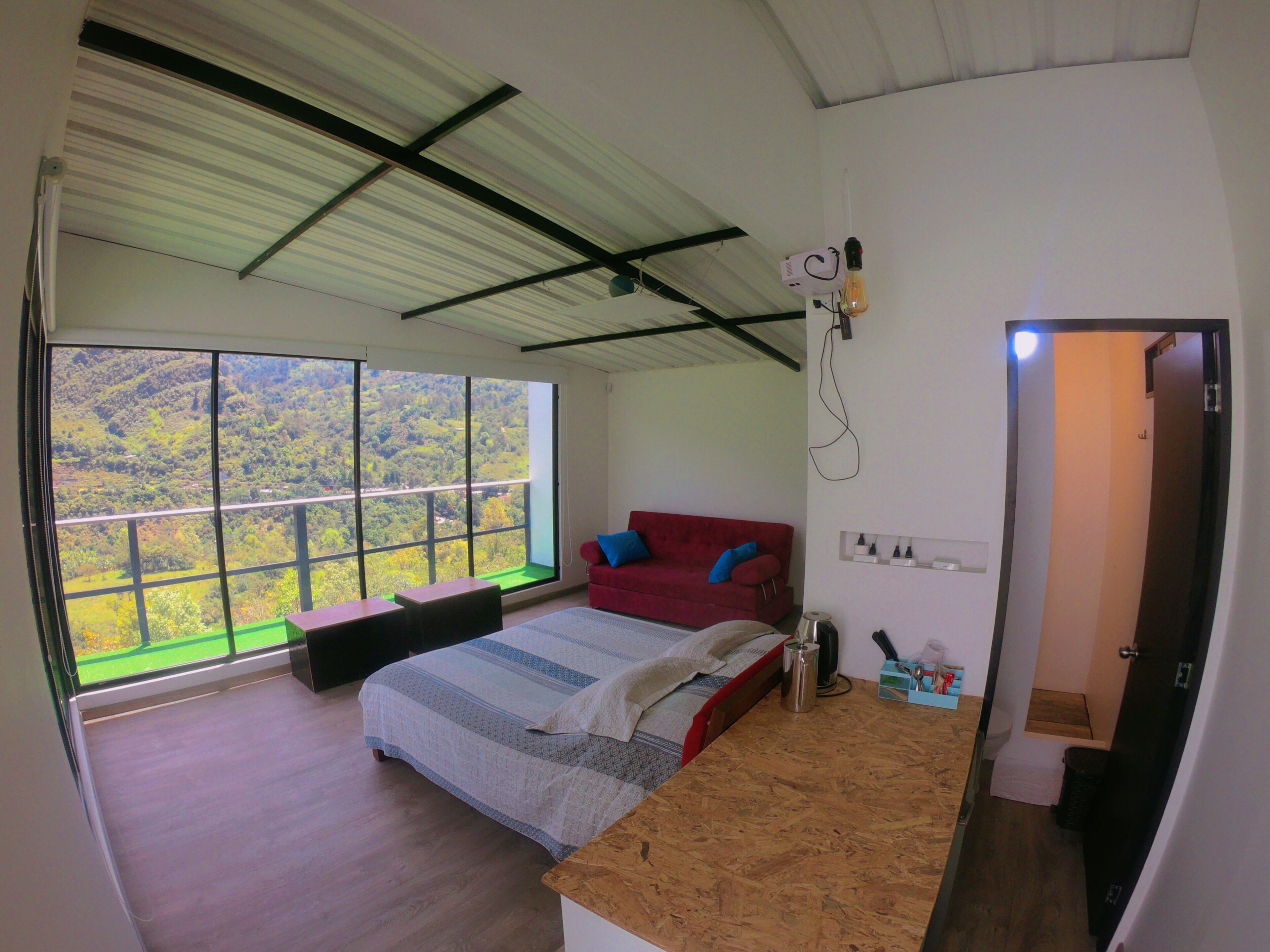 A bedroom with a large window, a red sofa, a wooden bed, and a small table.