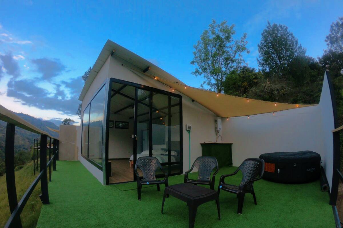 A modern outdoor seating area with a glass enclosure, a small table, and two chairs.
