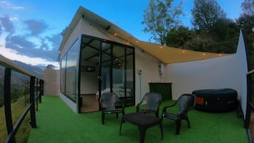 Ein moderner Außenbereich zum Sitzen mit Glasveranda, einem kleinen Tisch und zwei Stühlen.