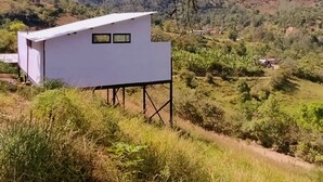 Un bâtiment blanc, de plain-pied et doté d’un toit plat, situé sur une colline verdoyante, avec une chaîne de montagnes en arrière-plan.