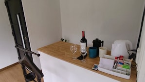 Un petit coin cuisine avec un plan de travail en bois, une bouteille de vin, deux verres à vin, une machine à café, une bouilloire et un plateau contenant divers objets.