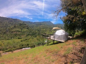 Una tienda blanca sobre una plataforma de madera con vistas a un valle exuberante y montañas.