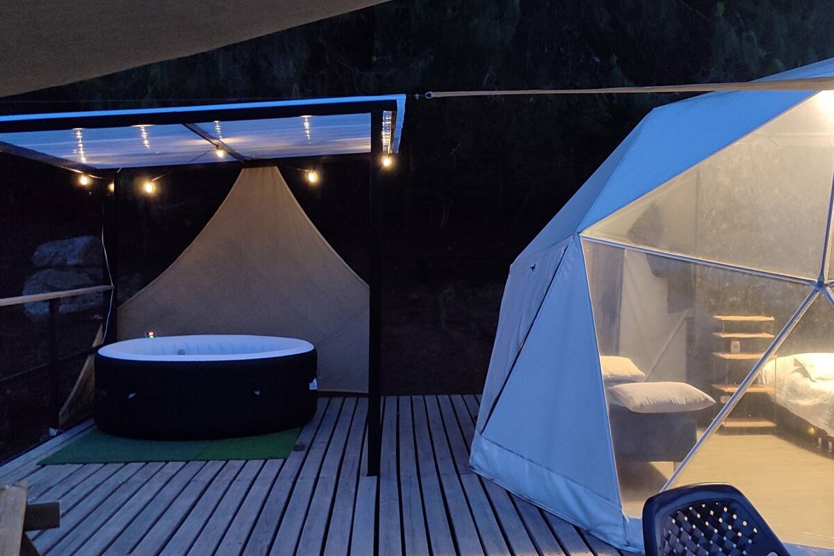 A tented accommodation with a hot tub, a bed, and a view of the night sky.