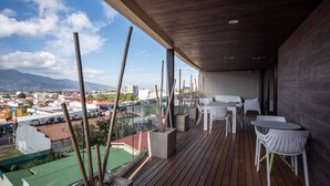 A balcony with wooden flooring, white chairs, and tables, overlooking a cityscape with buildings and mountains. - Digital Nomads Dream + Sauna (Curridabat)
