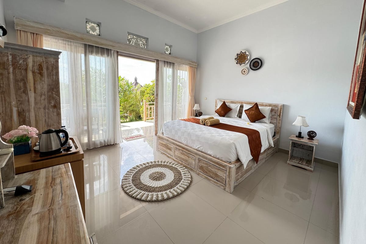 A spacious bedroom with a large bed, a wooden desk, a coffee maker, and a view of the outdoors.