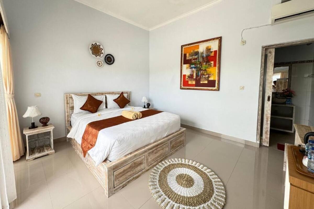 A bedroom with a bed, bedside table, lamp, and artwork on the wall.