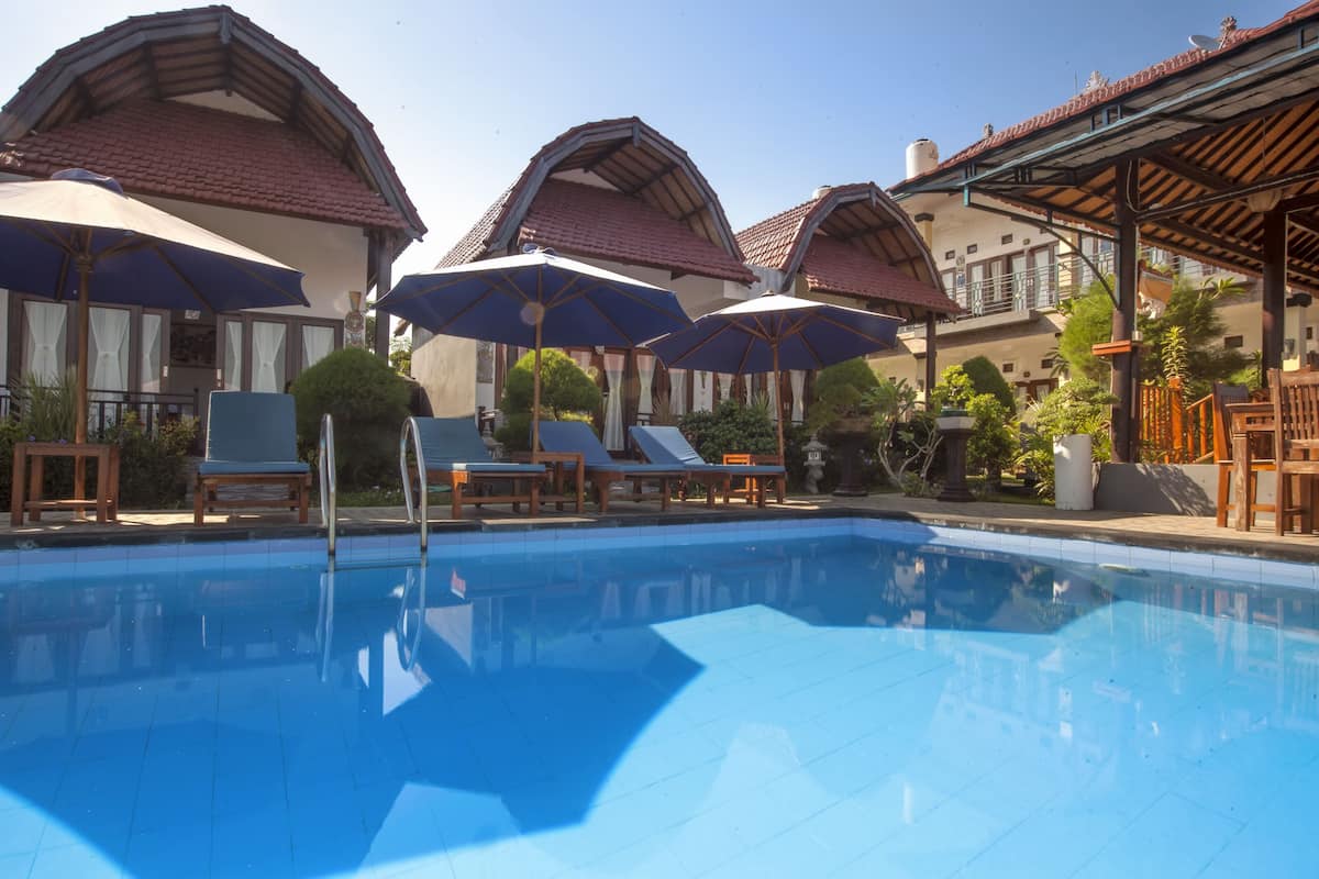 A swimming pool with lounge chairs and umbrellas, surrounded by buildings with red-tiled roofs.