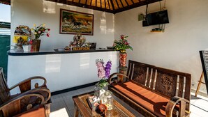 A reception area with a wooden bench, a reception desk, a painting, and a television mounted on the wall. - Kaylas Hill Resort (Penida Island)