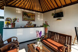 Un área de recepción con un banco de madera, un mostrador de recepción, un cuadro y un televisor montado en la pared.