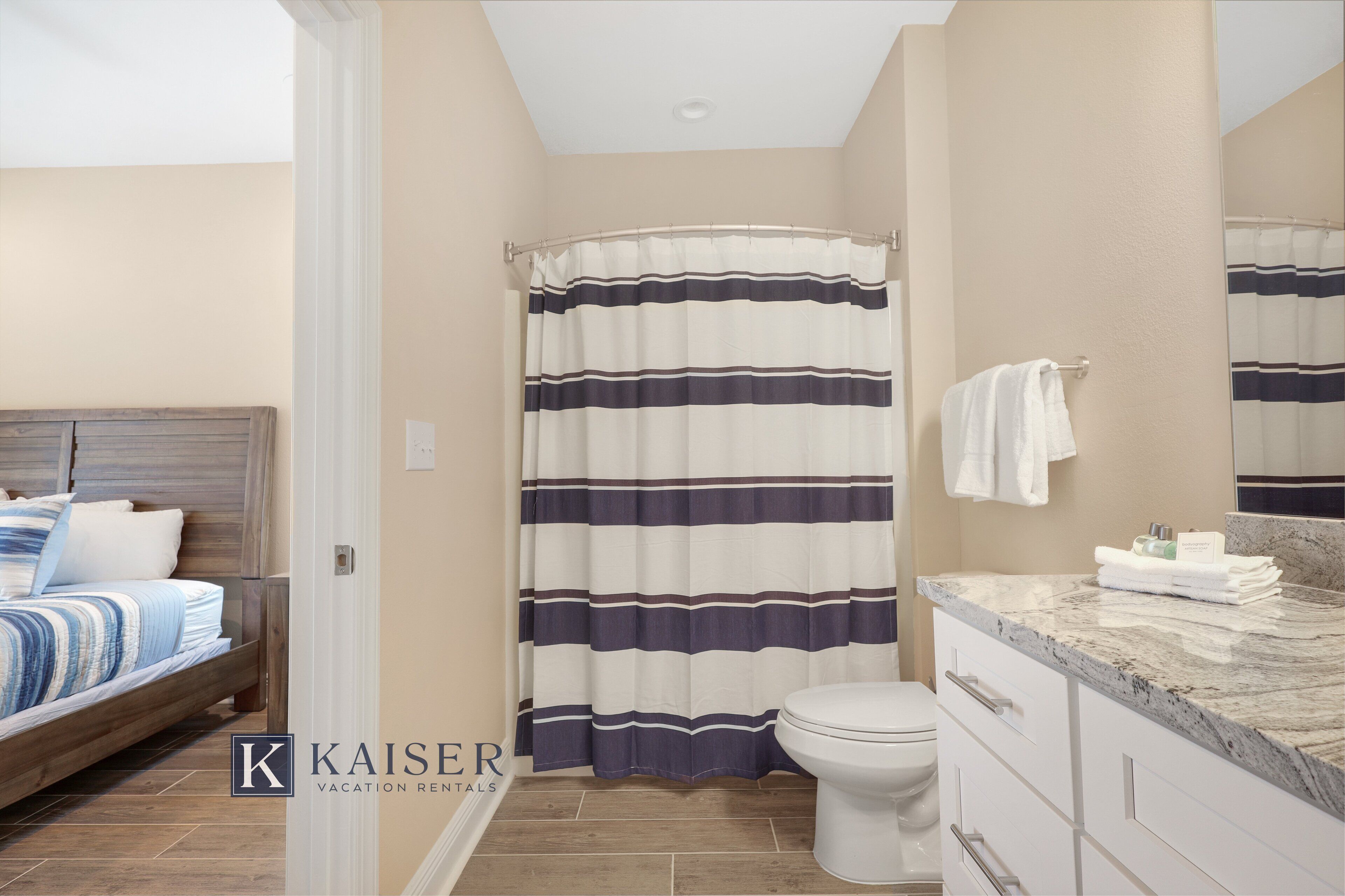 A bathroom with a shower curtain, toilet, and vanity with a marble countertop.