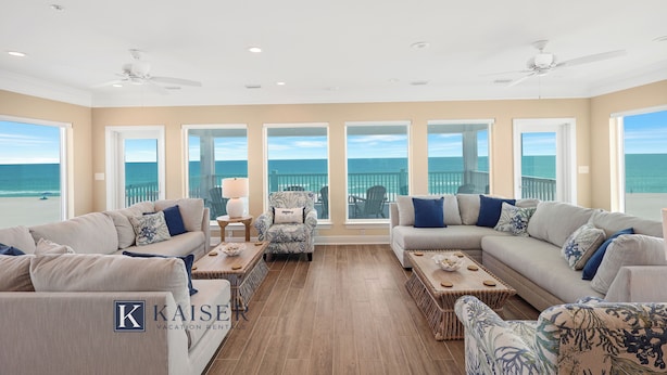 A spacious living room with a large window overlooking the ocean, a ceiling fan, and a chaise lounge.