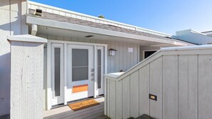 A building with a white exterior, a front door, a small porch, and a wooden fence. - Capitola Sea Breeze Retreat (Capitola)