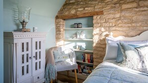 A bedroom with a stone wall, a white cabinet, a chair, a bookshelf, and a bed with floral bedding.