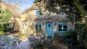 A stone house with a blue door, a small garden with a table and chairs, and a gravel path.