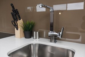 A modern kitchen with a stainless steel sink, a knife block, a potted plant, and a sleek faucet.