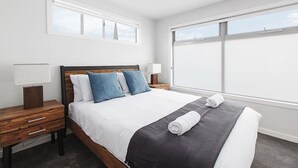 Una habitación de hotel moderna con una cama grande, dos mesitas de noche y un gran ventanal con vistas.