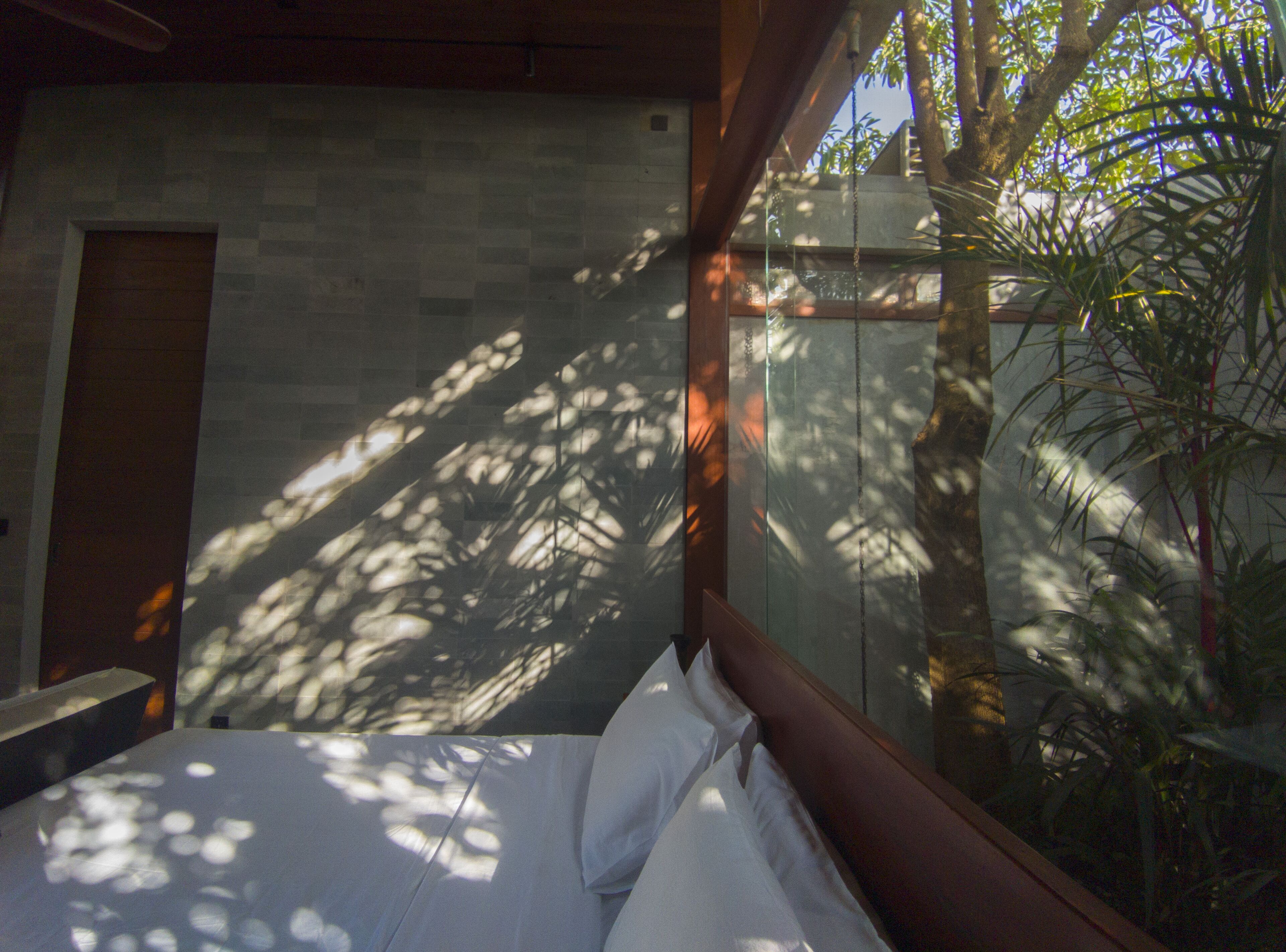 A bedroom with a bed, a wooden headboard, a stone wall, and a window with a view of trees.