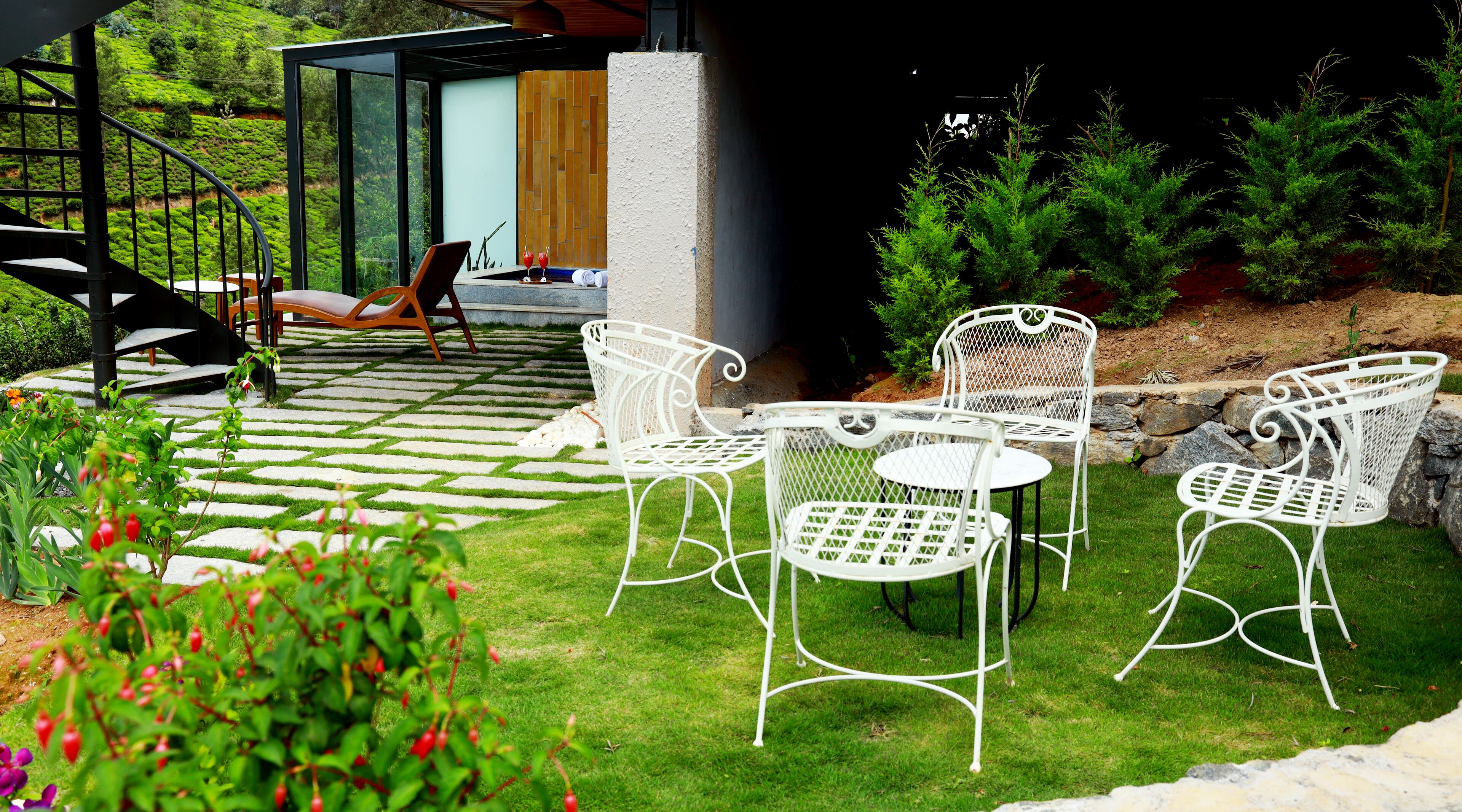 Une terrasse avec des chaises et une table en métal blanc, entourée d’un mur de pierre et de verdure.